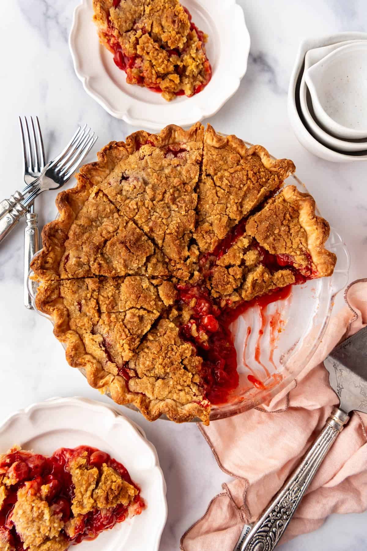 An overhead image of a cherry crumb pie that has been sliced with some pieces removed.