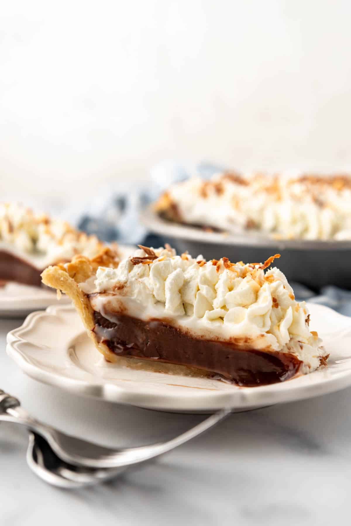 A slice of homemade haupia pie on a plate with two forks in front of it.