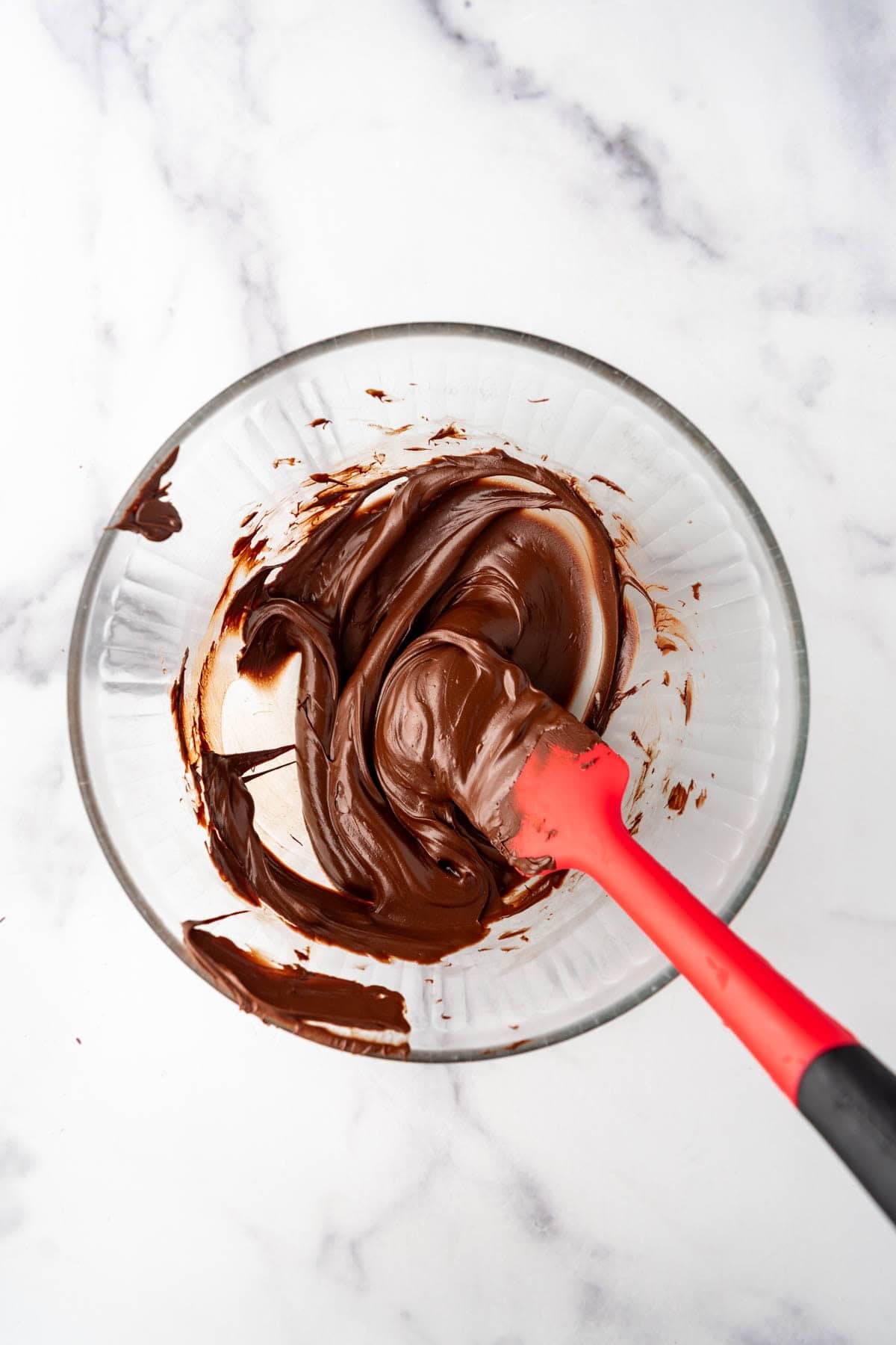 Melted chocolate in a glass bowl with a spatula.