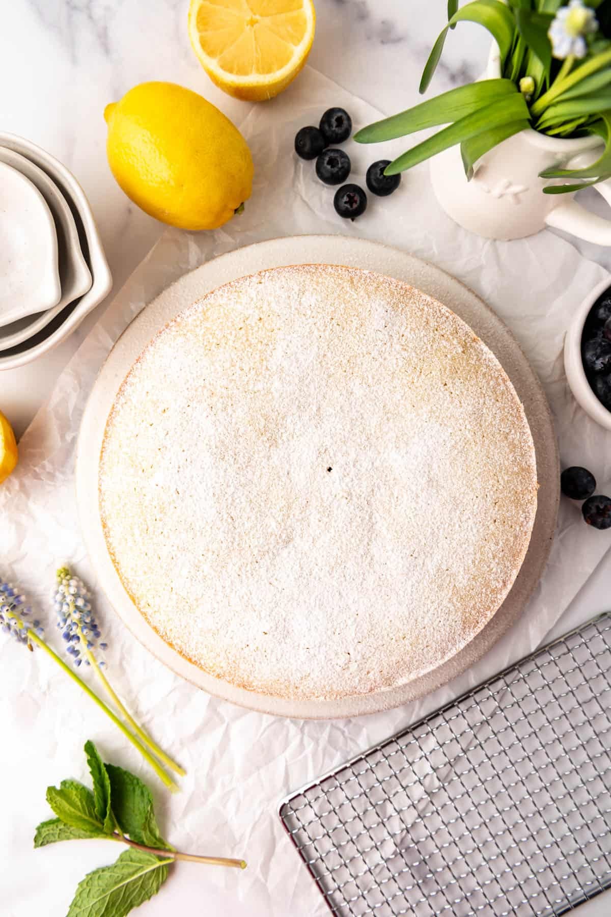 An overhead image of a lemon olive oil cake next to lemons, mint, and blueberries.