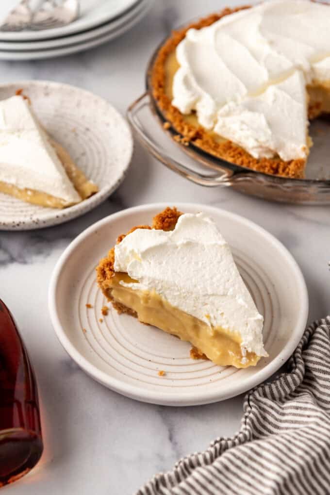 A slice of maple cream pie on a plate with the rest of the pie in the background.