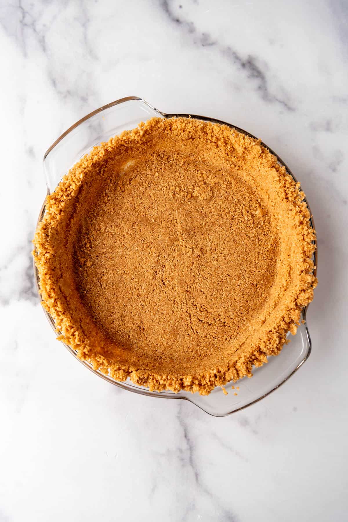 An overhead image of a homemade graham cracker crust in a glass pie plate.