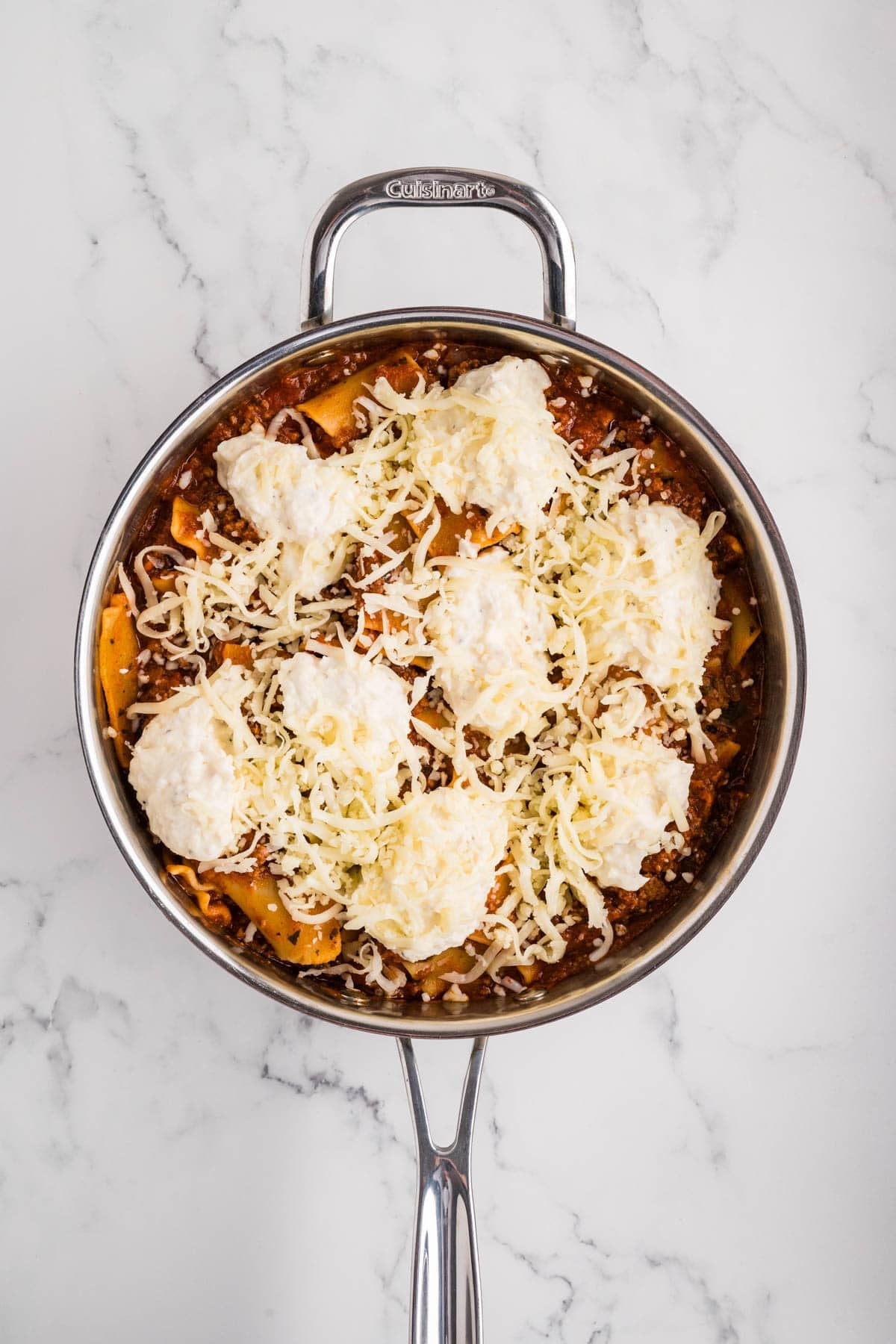 Shredded mozzarella cheese sprinkled over a skillet full of lasagna.