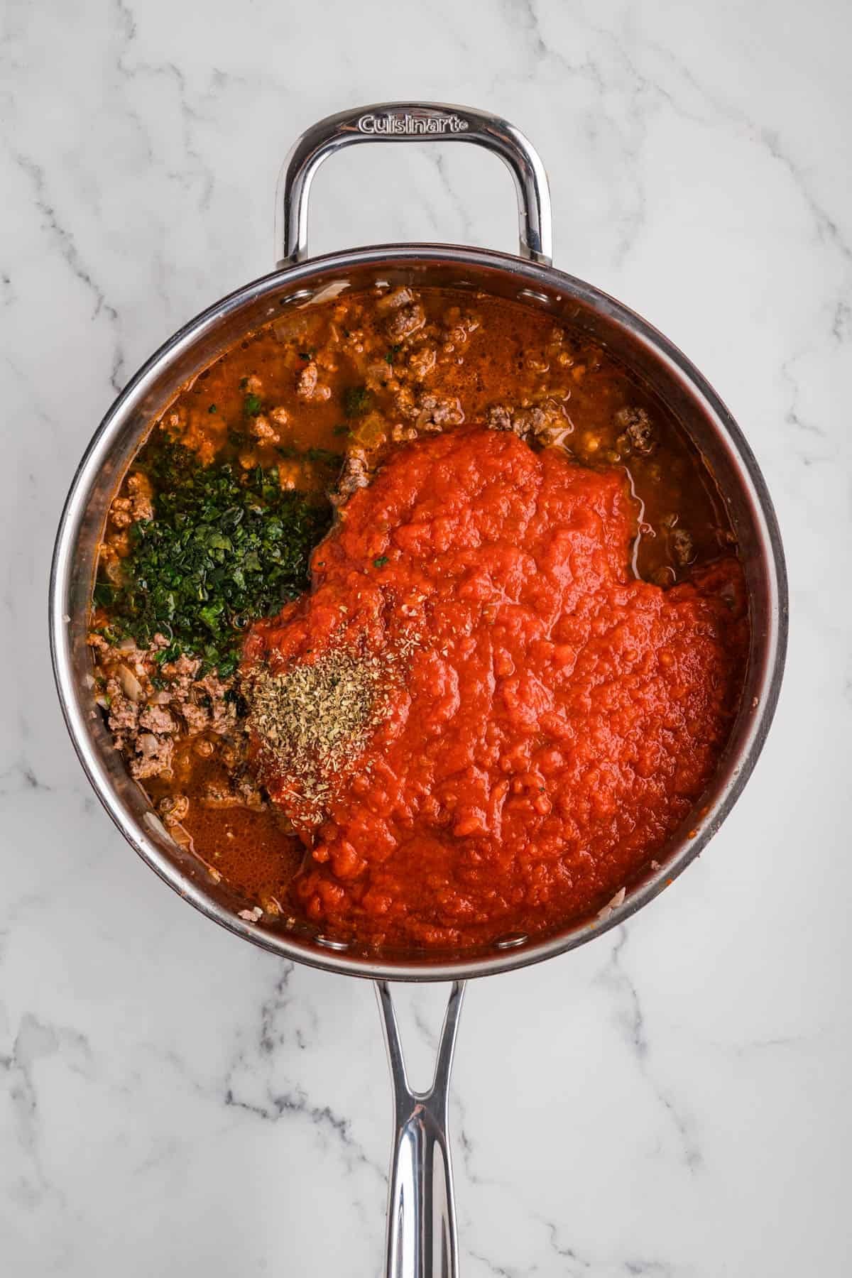 Adding crushed tomatoes and spices to a pan of ground beef.