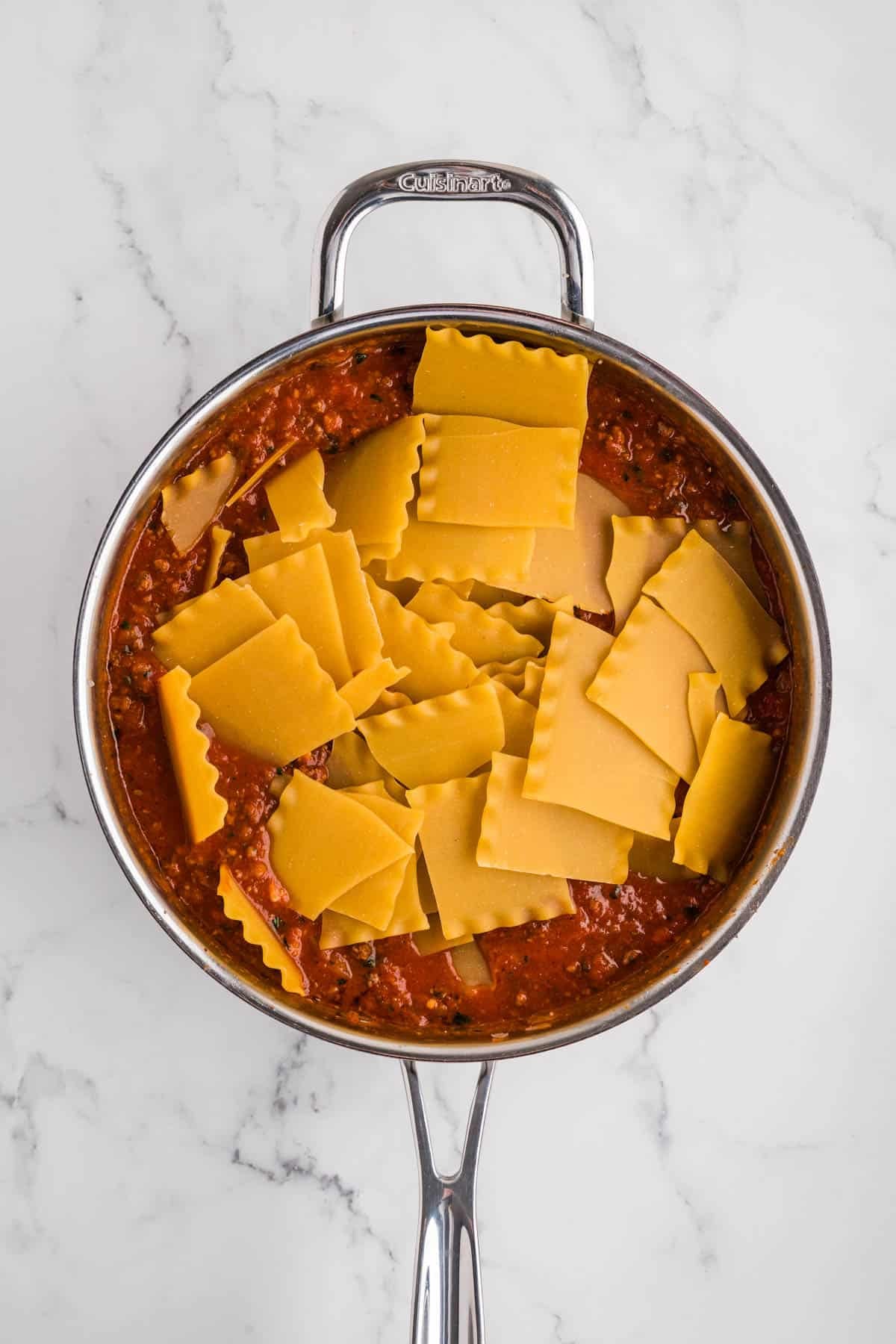Broken lasagna noodles being added to sauce in a pan.