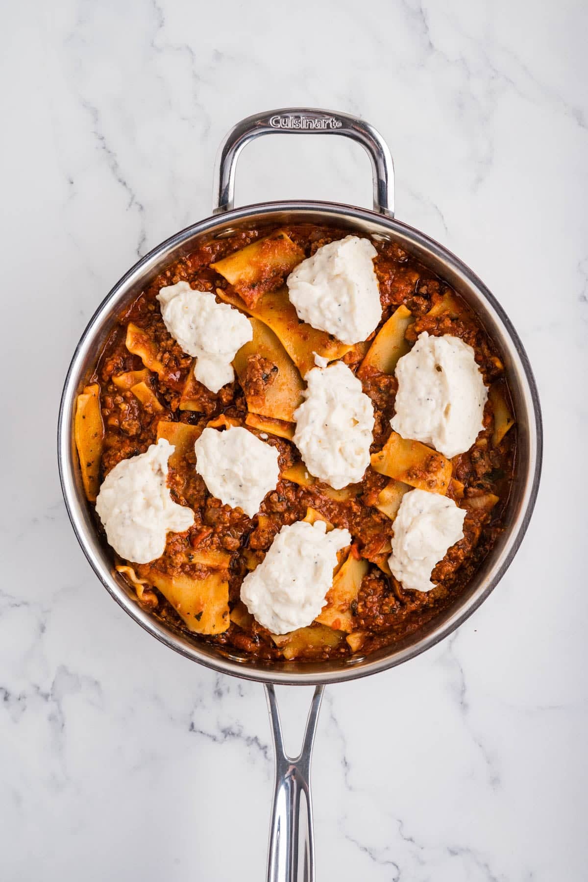 Adding dollops of cheese mixture to a skillet lasagna.