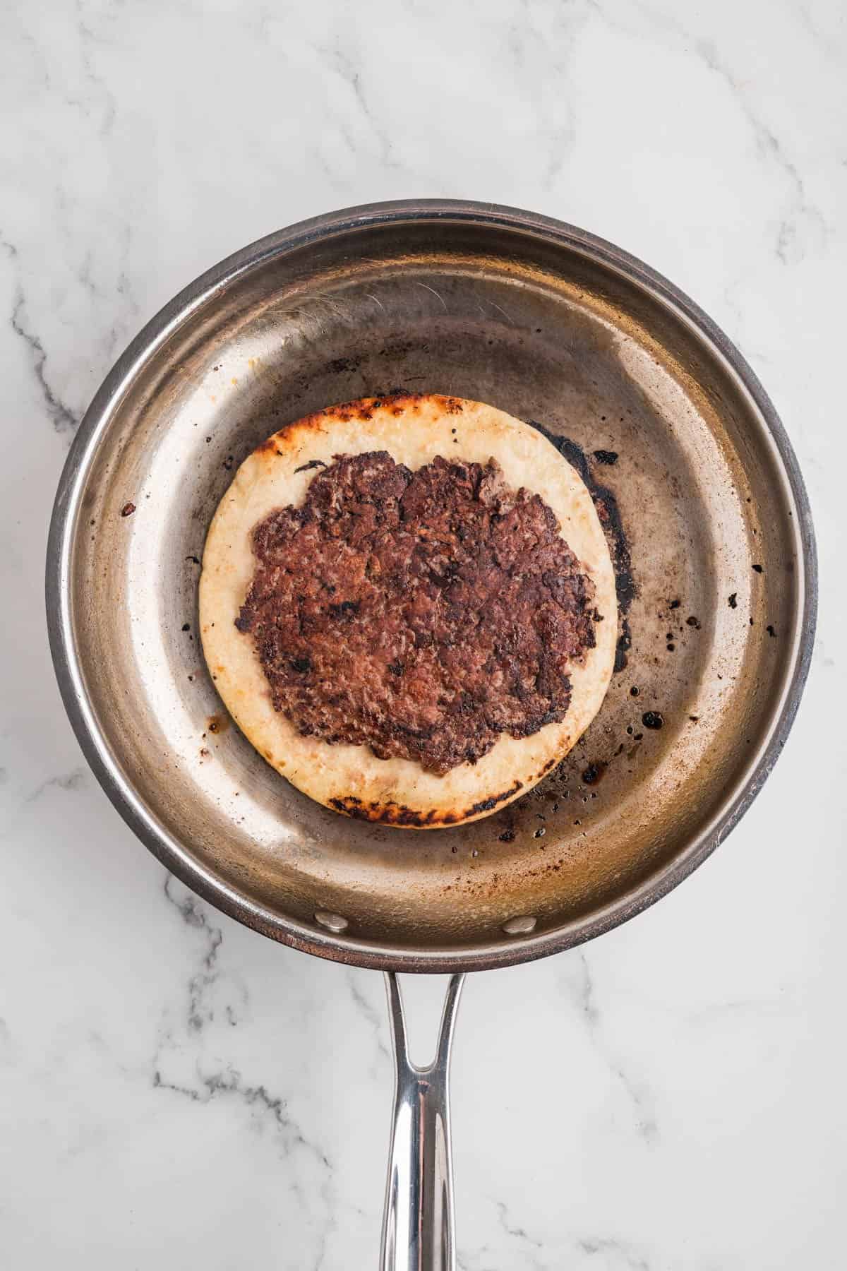 Browned ground beef on top of a tortilla in a large skillet.
