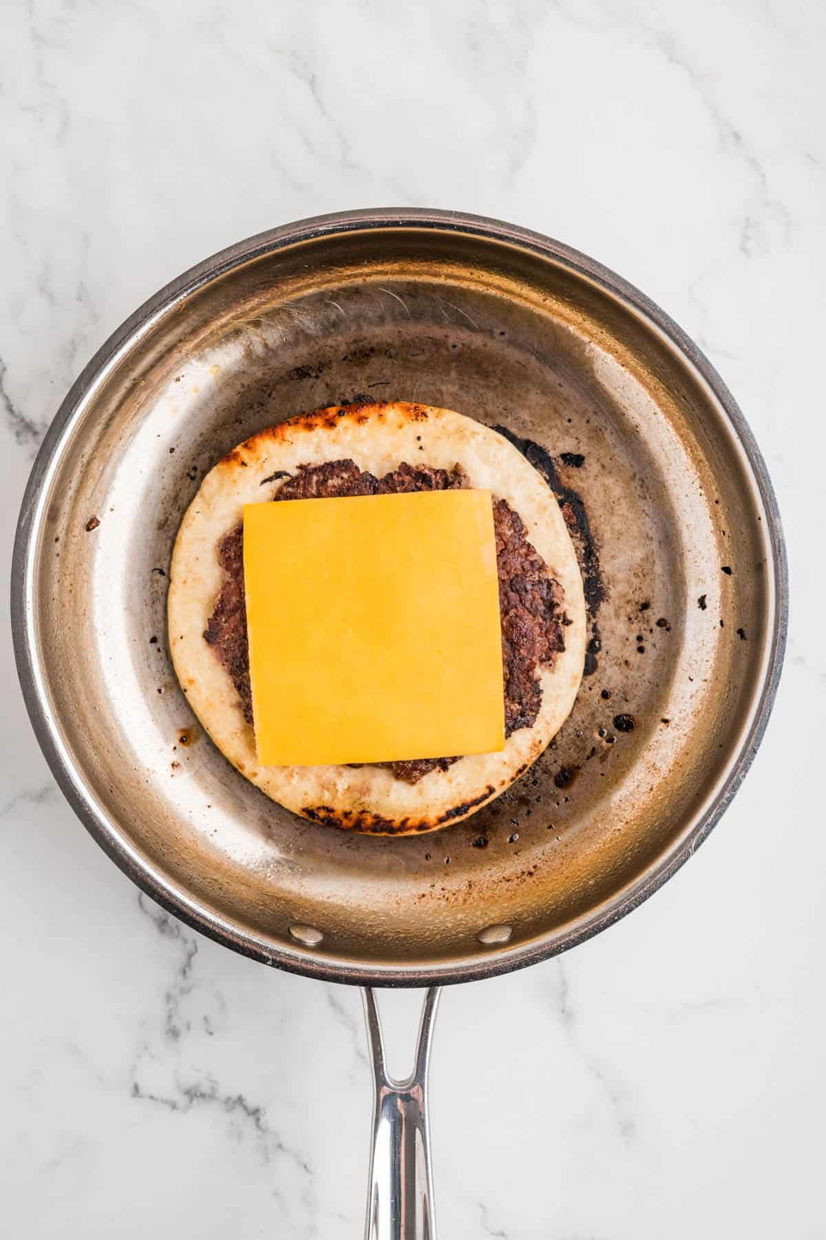 A slice of cheese on top of a smash burger taco.