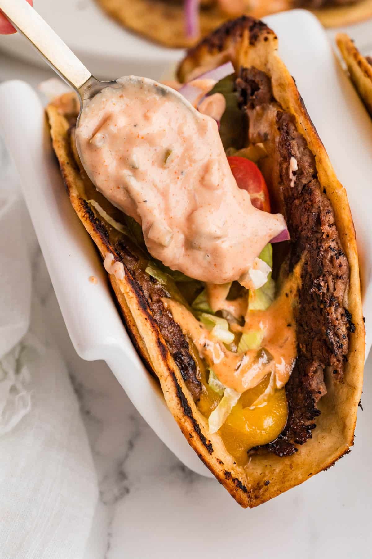 Burger sauce being spooned over a smash burger taco.