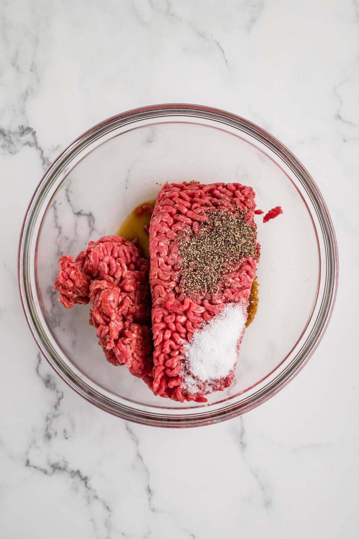 An overhead image of ground beef in a bowl with salt, pepper, and Worcestershire sauce.