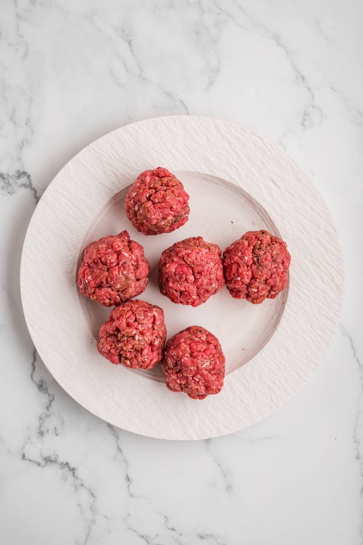 Balls of ground beef mixture on a white plate.