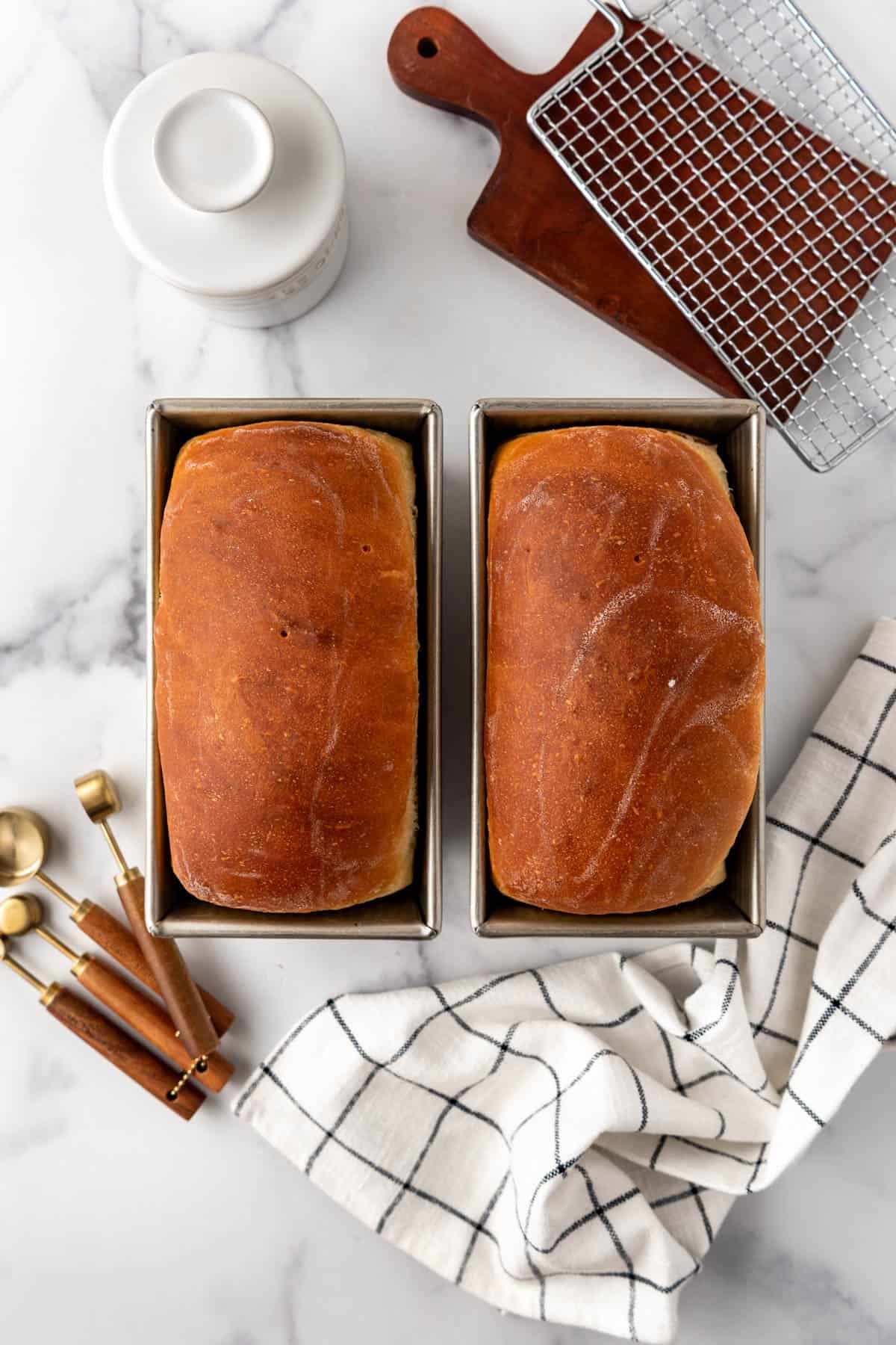 Two baked loaves of sourdough sandwich bread in their pans.