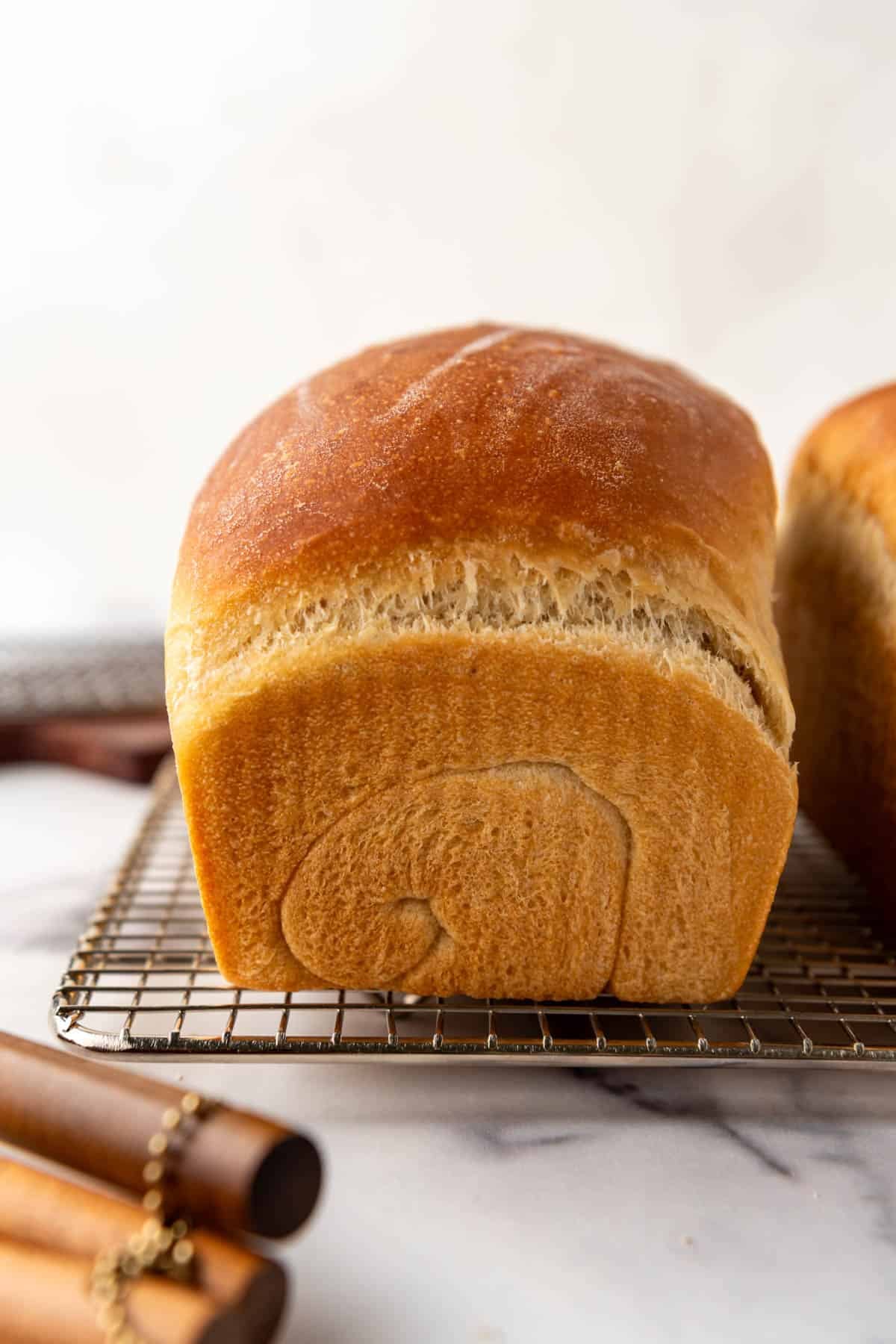 A loaf of soft sourdough sandwich bread on a cooling rack.