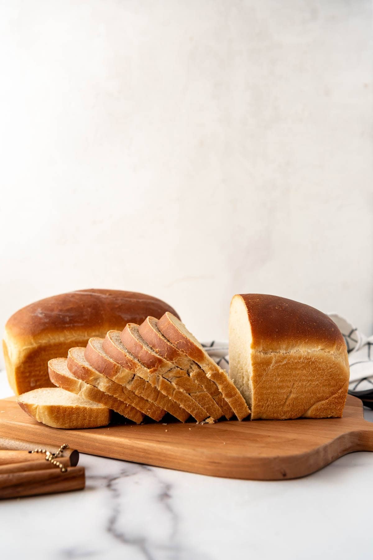 An image of a partially sliced loaf of soft sourdough sandwich bread on a wooden cutting board.
