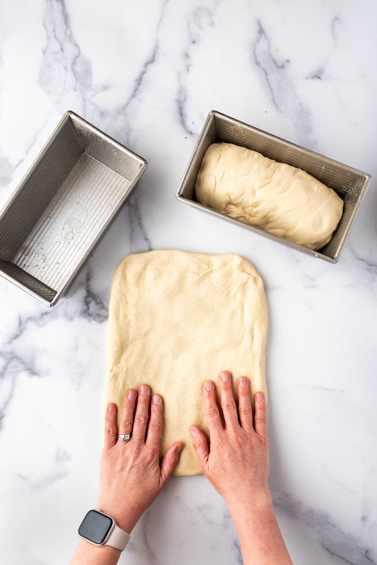 Hands pressing bread dough into a rectangle.