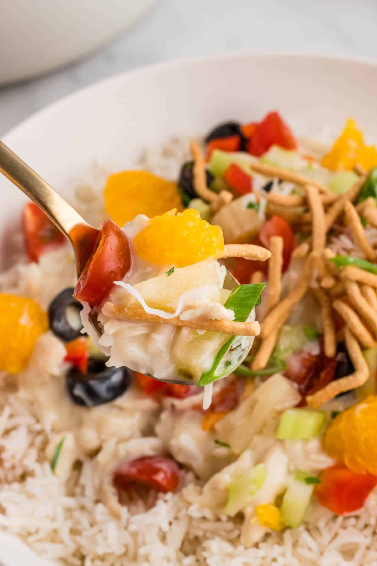 A forkful of Hawaiian haystacks with crunchy chow mein noodles, mandarin oranges, and other toppings.