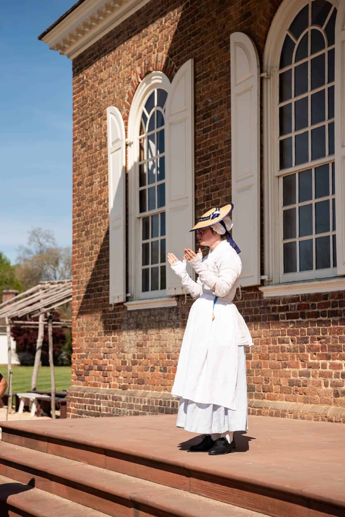A woman in colonial dress standing on the steps of the courthouse in Colonial Williamsburg.