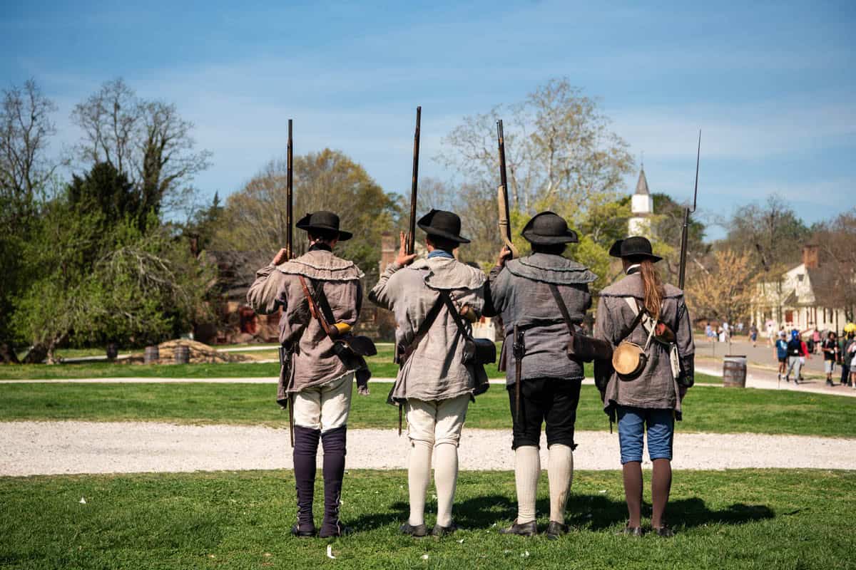 Soldiers in revolutionary war colonial garb standing at attention with muskets in Colonial Williamsburg.