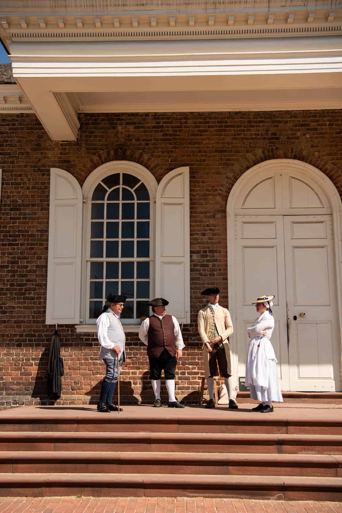 Four people in period costumes standing on the steps of the courthouse in Colonial Williamsburg.