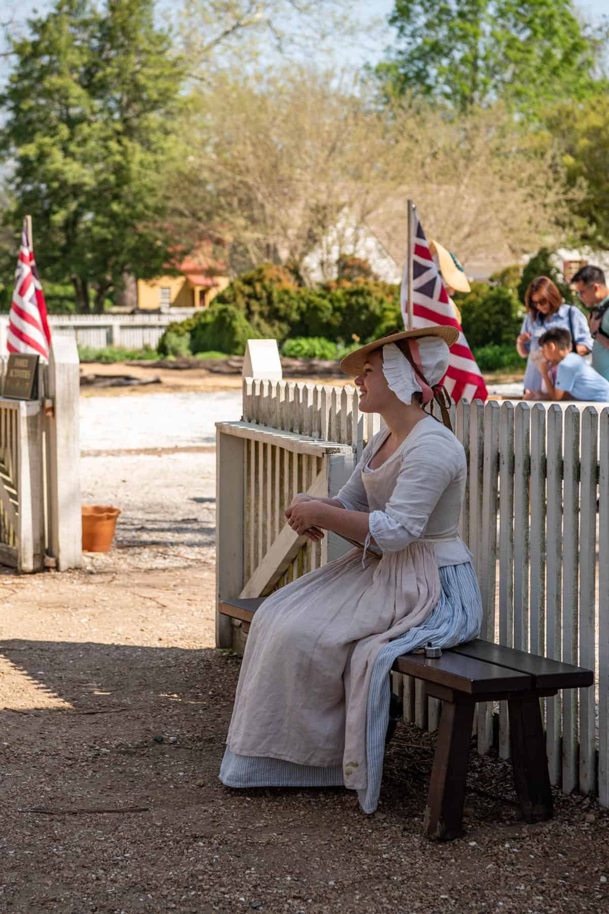 A woman in colonial dress sitting on a bench in Colonial Williamsburg.
