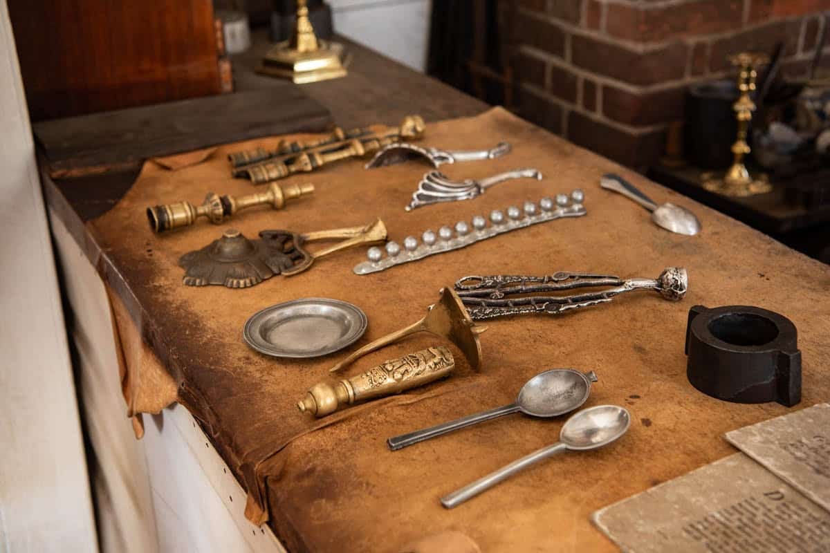 Colonial metal goods like spoons and door handles lying on a leather covered table.