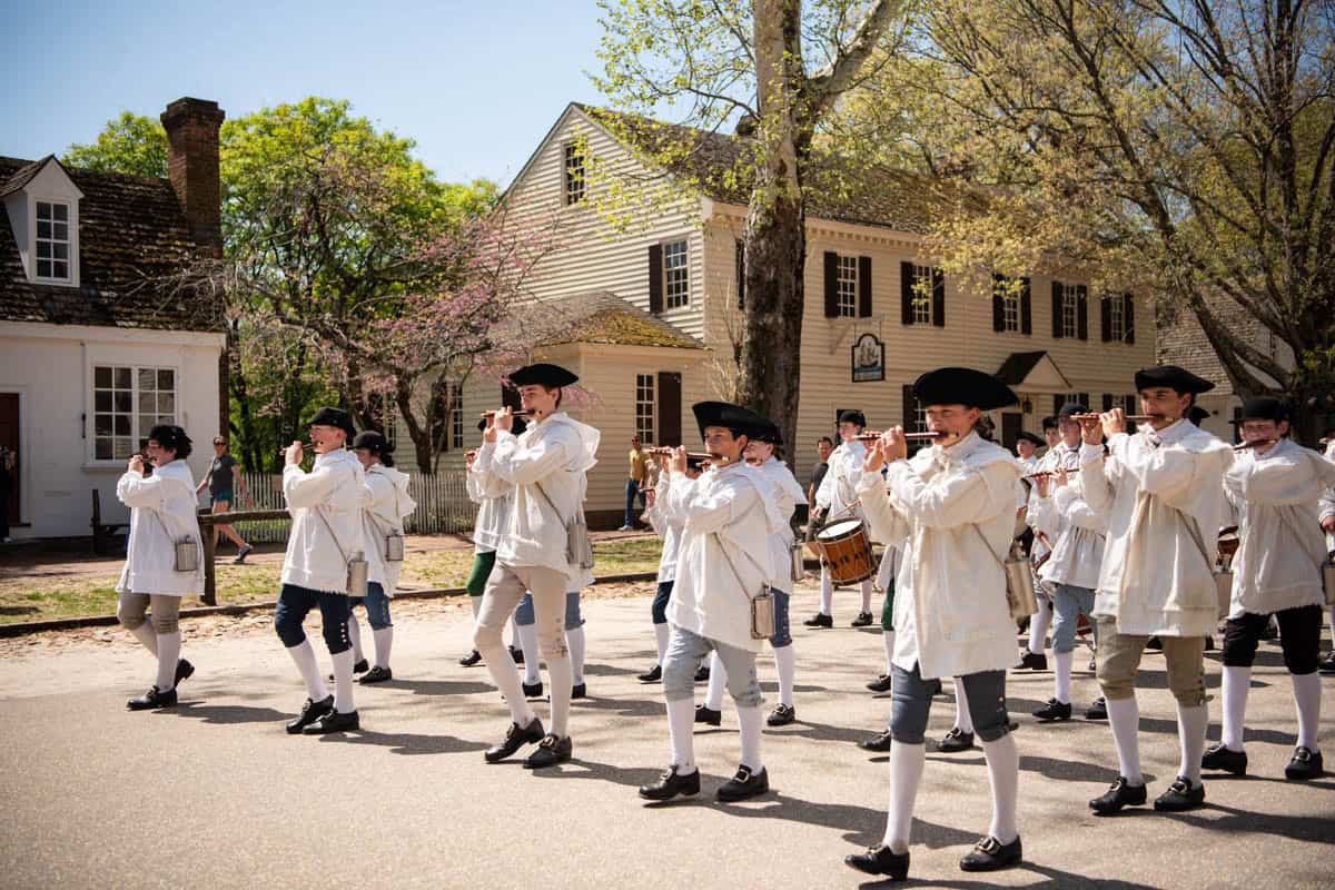A marching band in colonial era attire marching and playing fifes in Colonial Williamsburg.