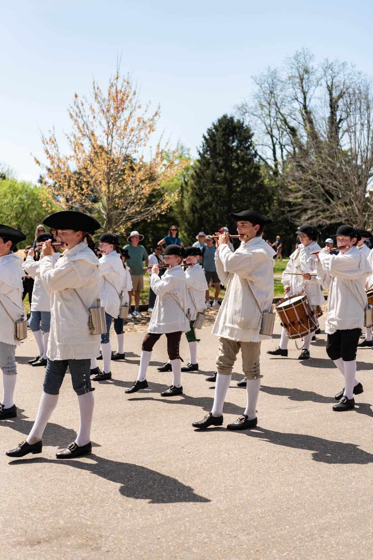 A marching band in colonial era attire marching and playing fifes in Colonial Williamsburg.
