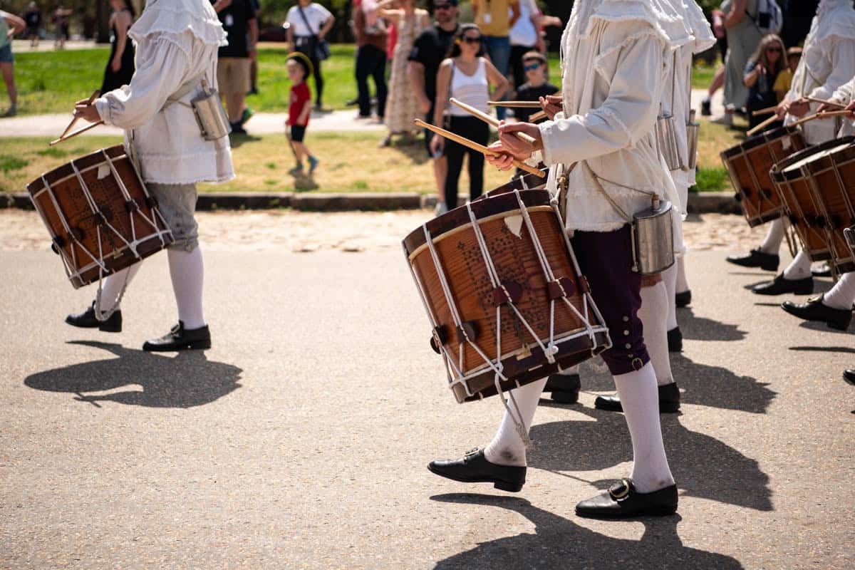 A close-up image of a drum being played by a marching band in revolutionary clothing in Colonial Williamsburg.