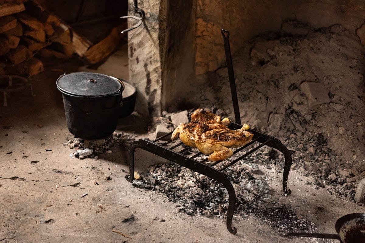 An image of a chicken roasting over coals next to an iron pot of pottage at Jamestown Settlement museum.