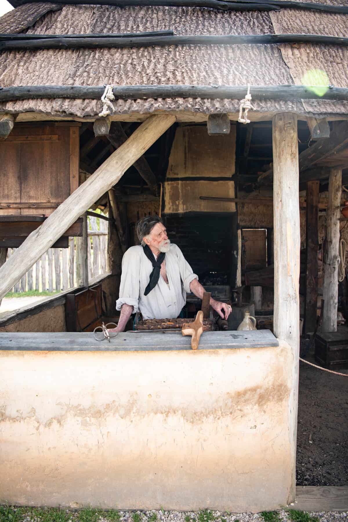 A man in a blacksmith booth in colonial clothing in Jamestown, Virginia.