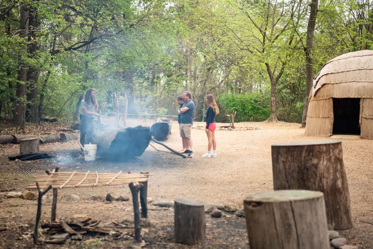 An image of a family watching a canoe being created from a log being burned to hollow it out.