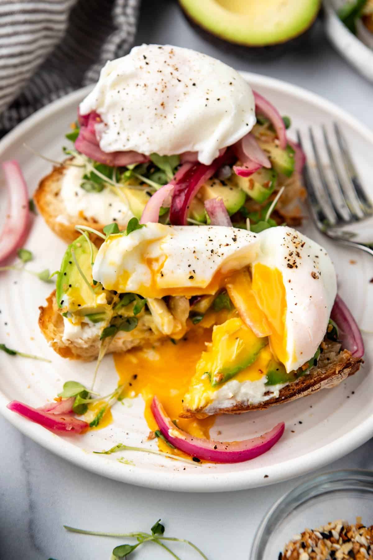 Avocado toast with a poached egg on top that has been sliced into with a runny yolk spilling out.