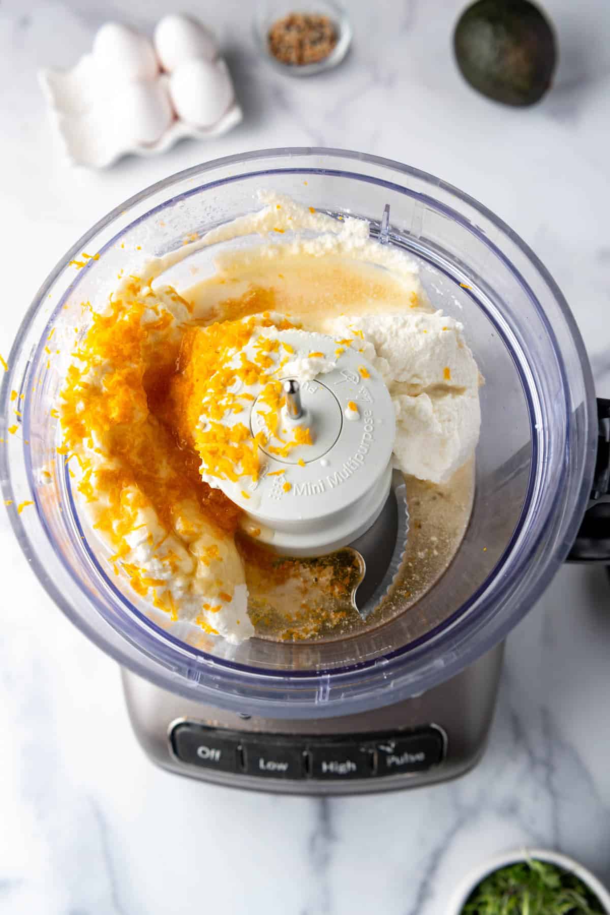 An image of a food processor with ricotta cheese, honey, and orange zest in it.