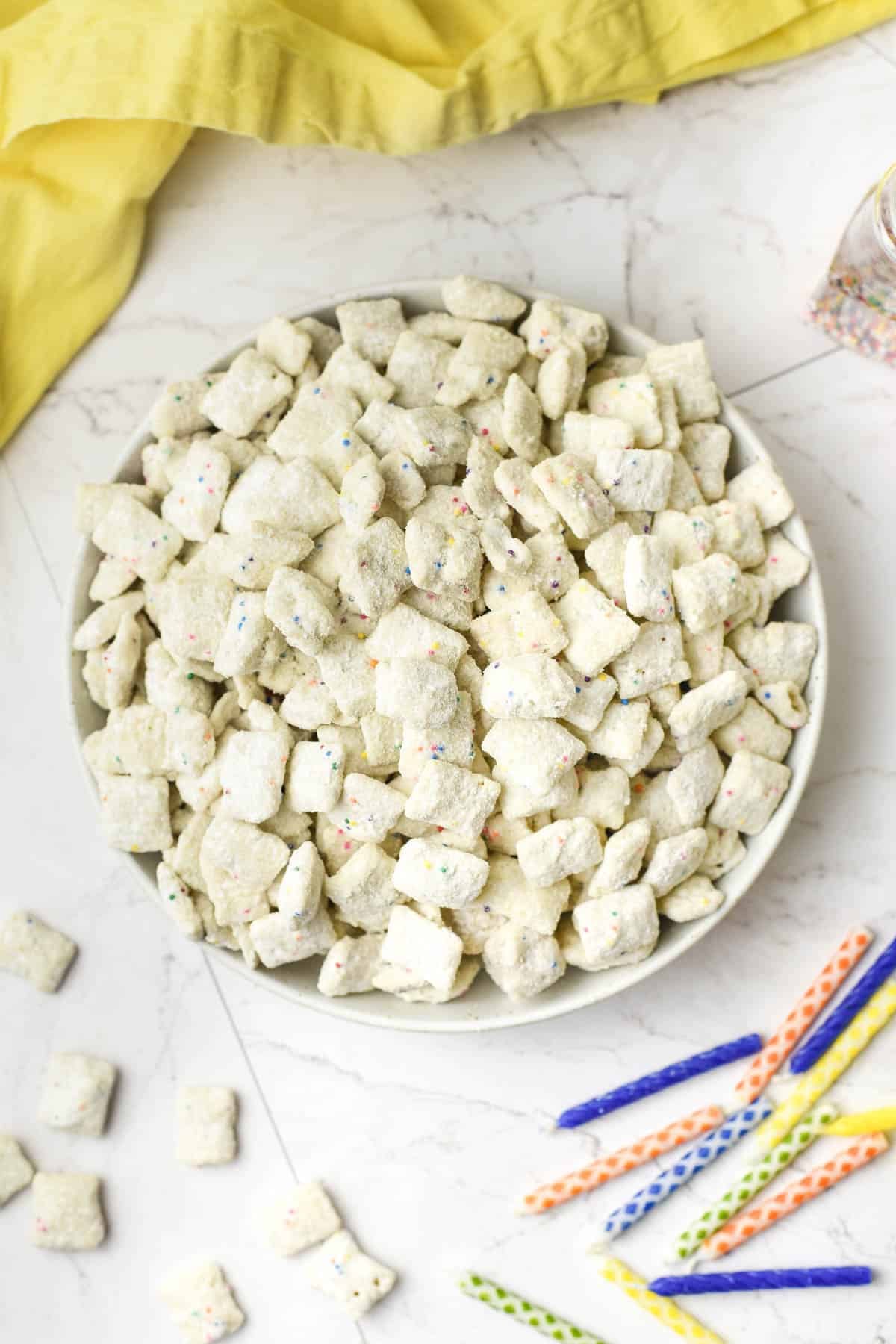 An overhead image of a bowl of cake batter puppy chow with birthday candles nearby.