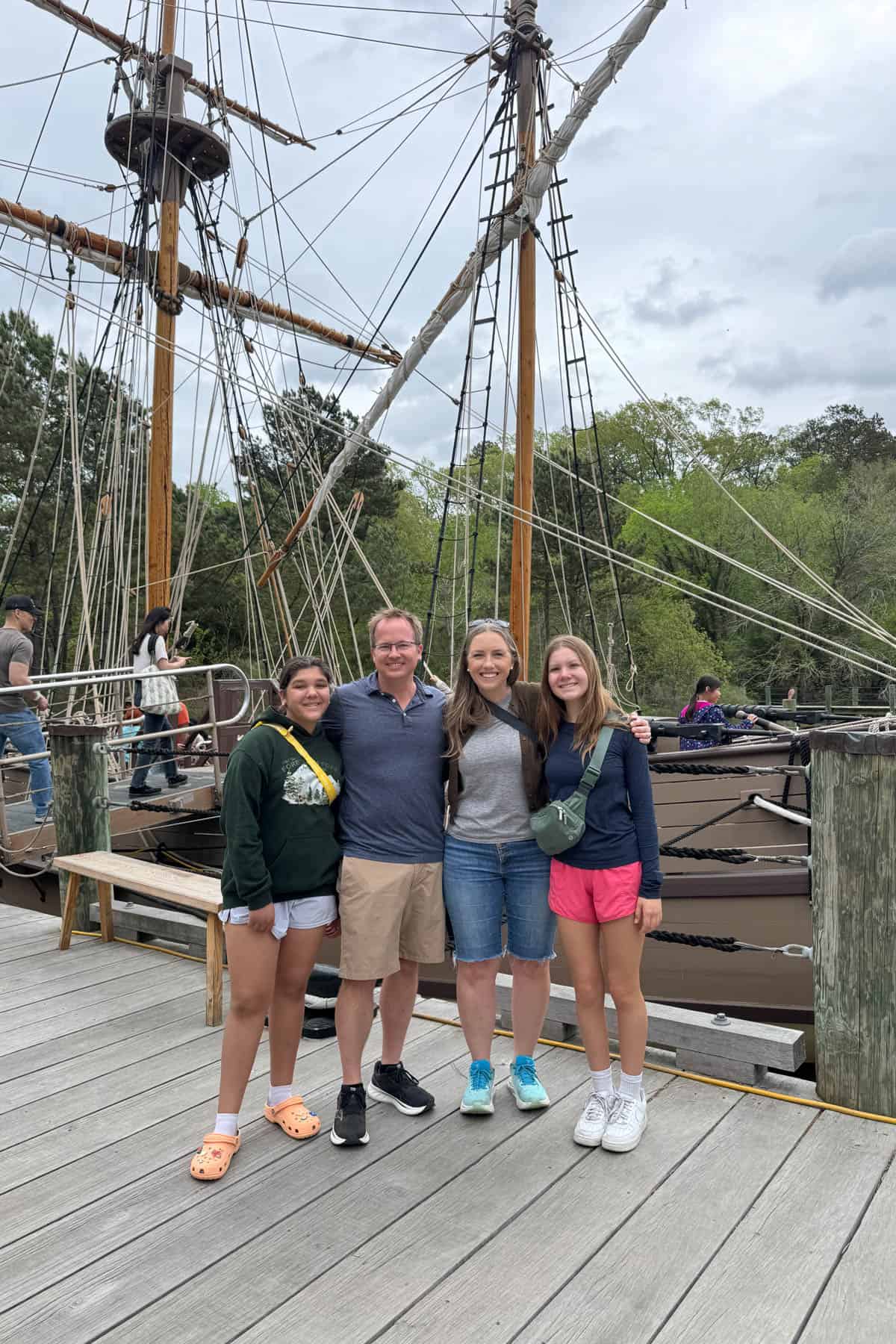 A family in front of a historical replica boat from Jamestown Settlement.