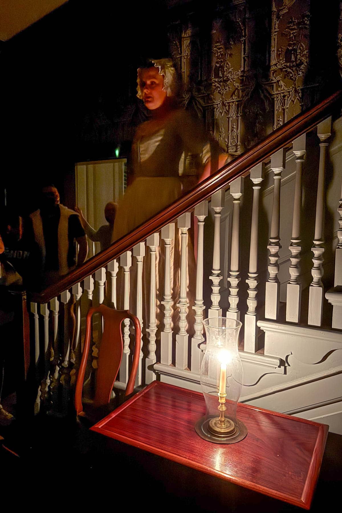 A woman standing on stairs in a dark room lit only by a candle.