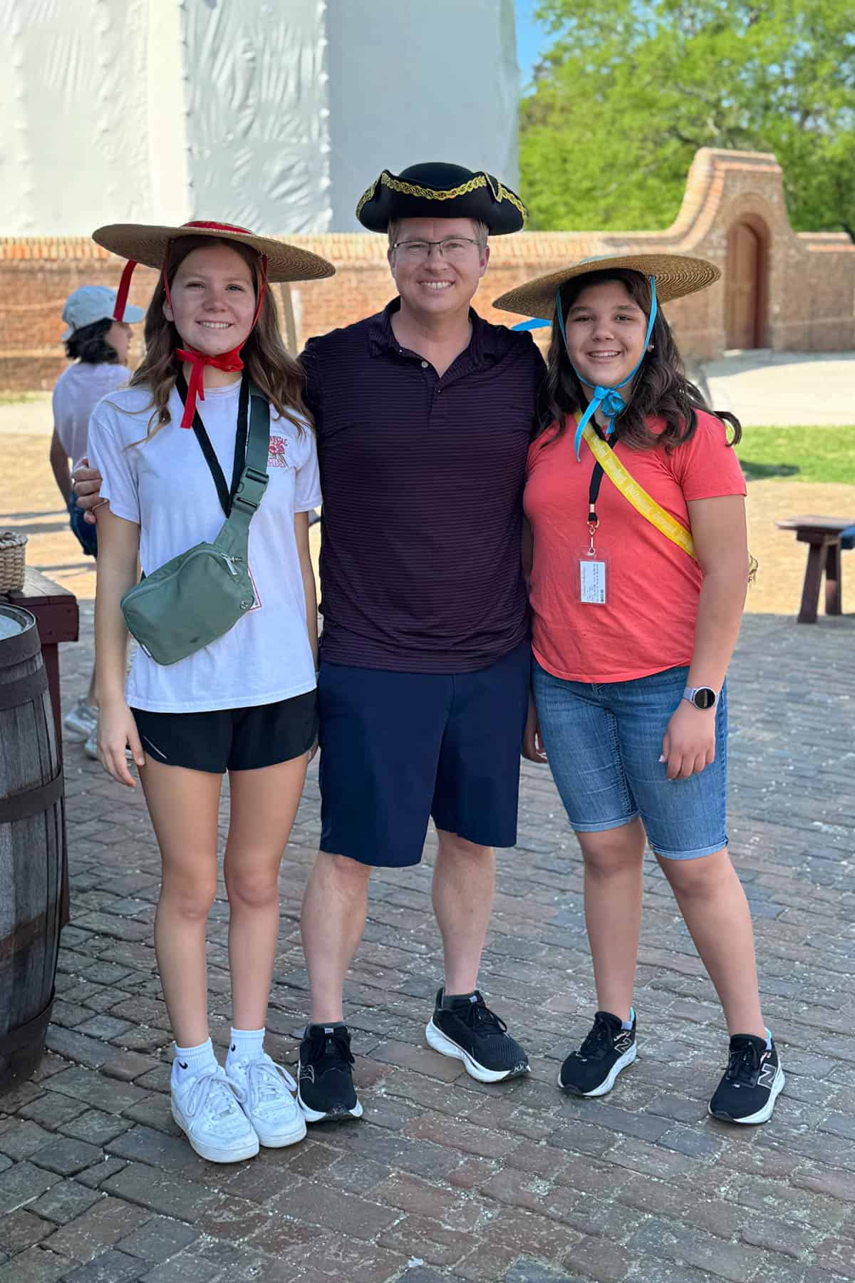 A dad and two daughters wearing colonial hats.