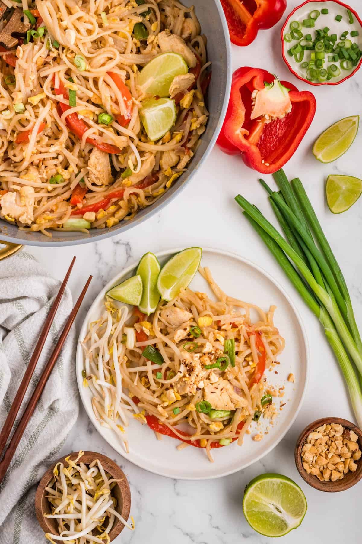 A plate of pad thai next to the rest of the food in a pan.