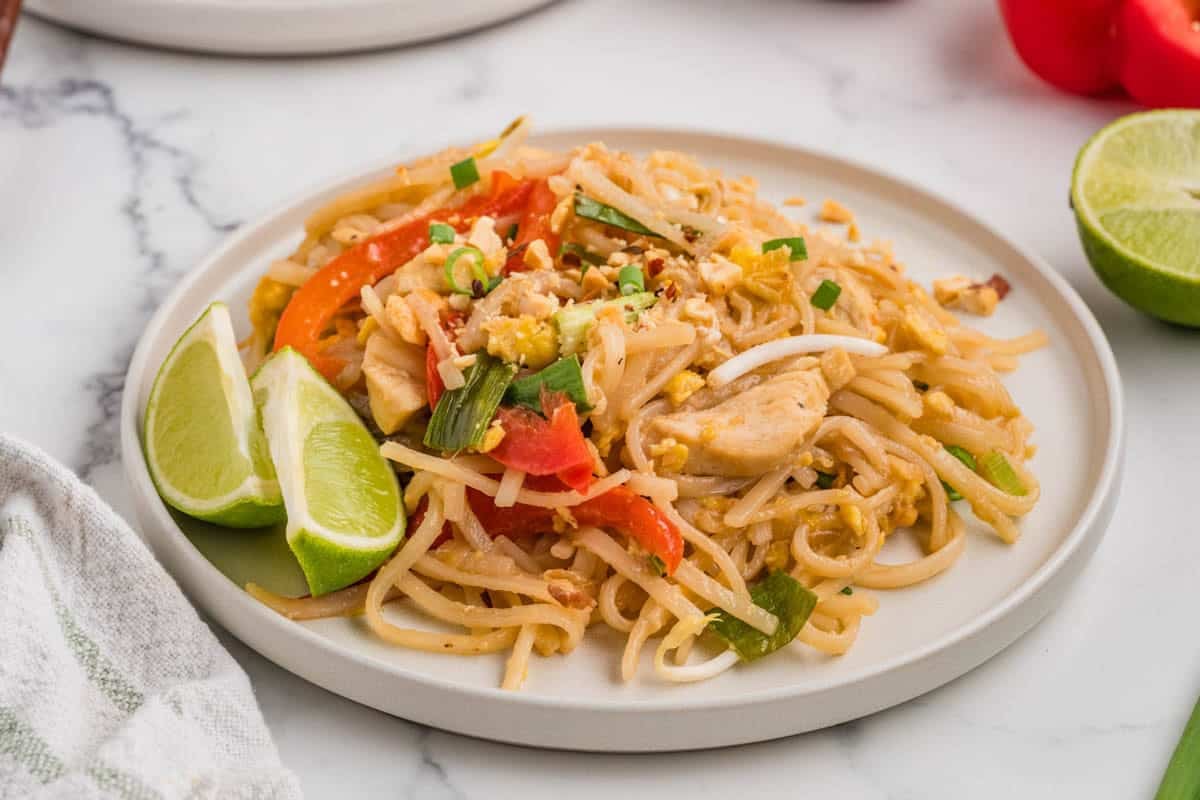A plate of pad thai garnished with lime wedges.