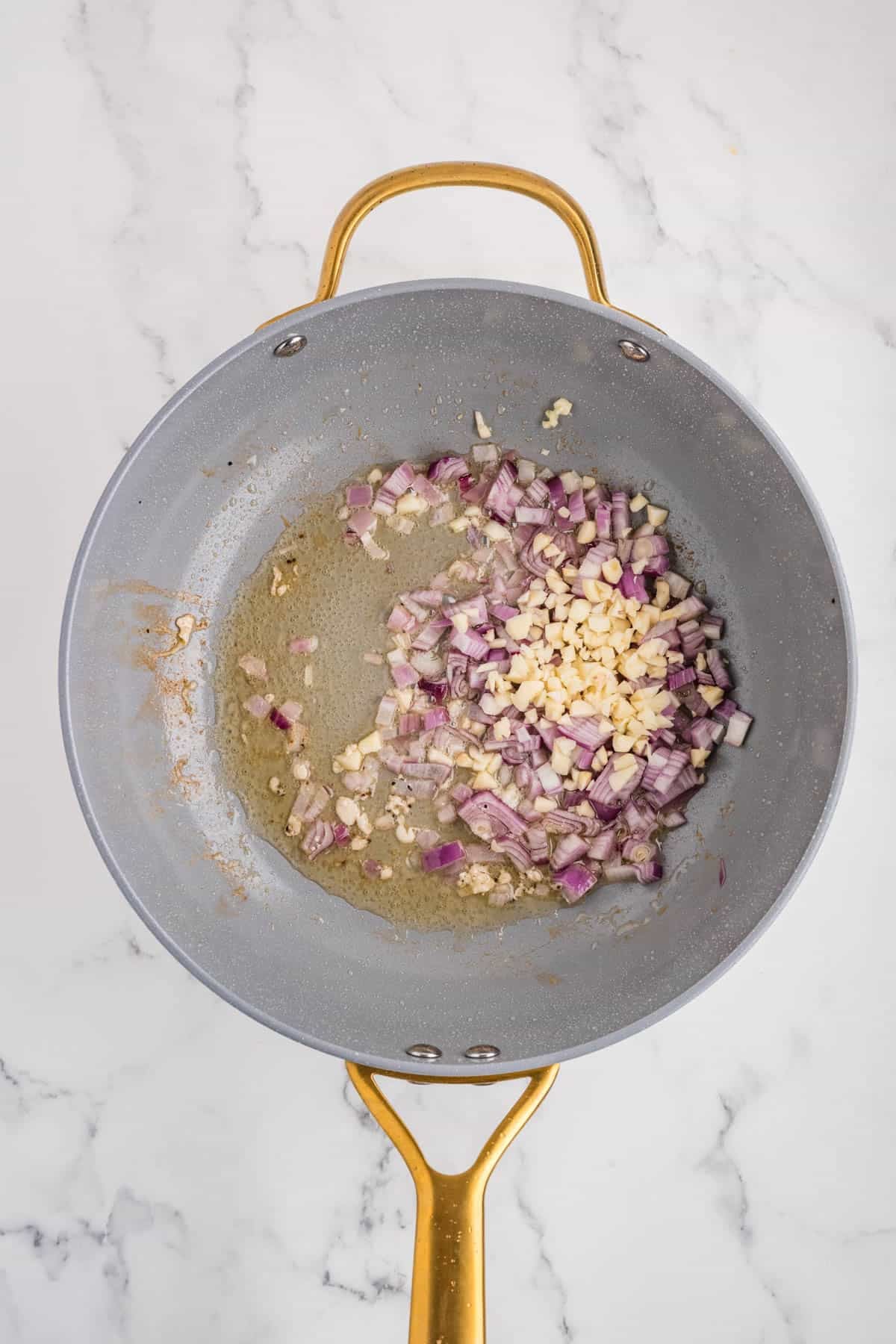 Chopped onions and garlic being cooked in a pan with oil.