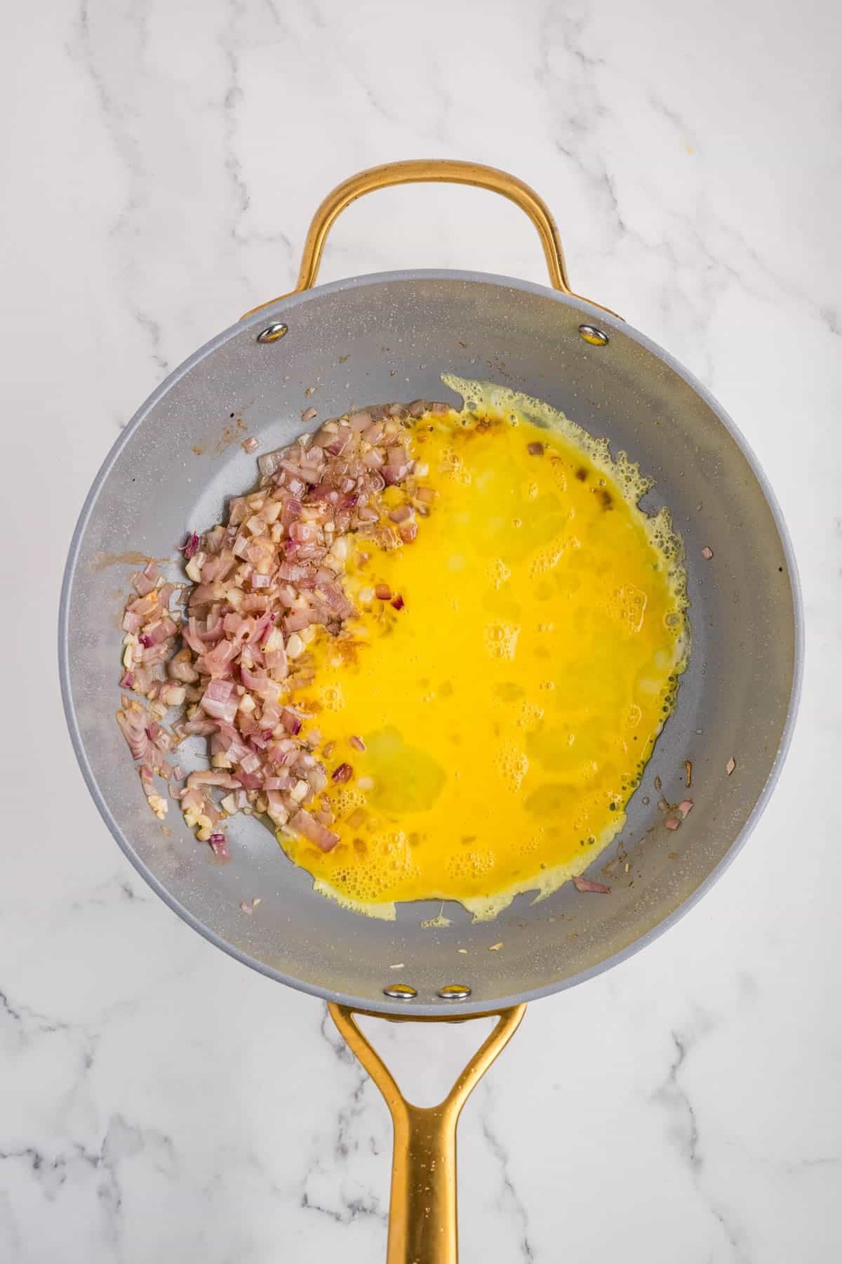 Adding beaten eggs to sauteed onions in a pan.