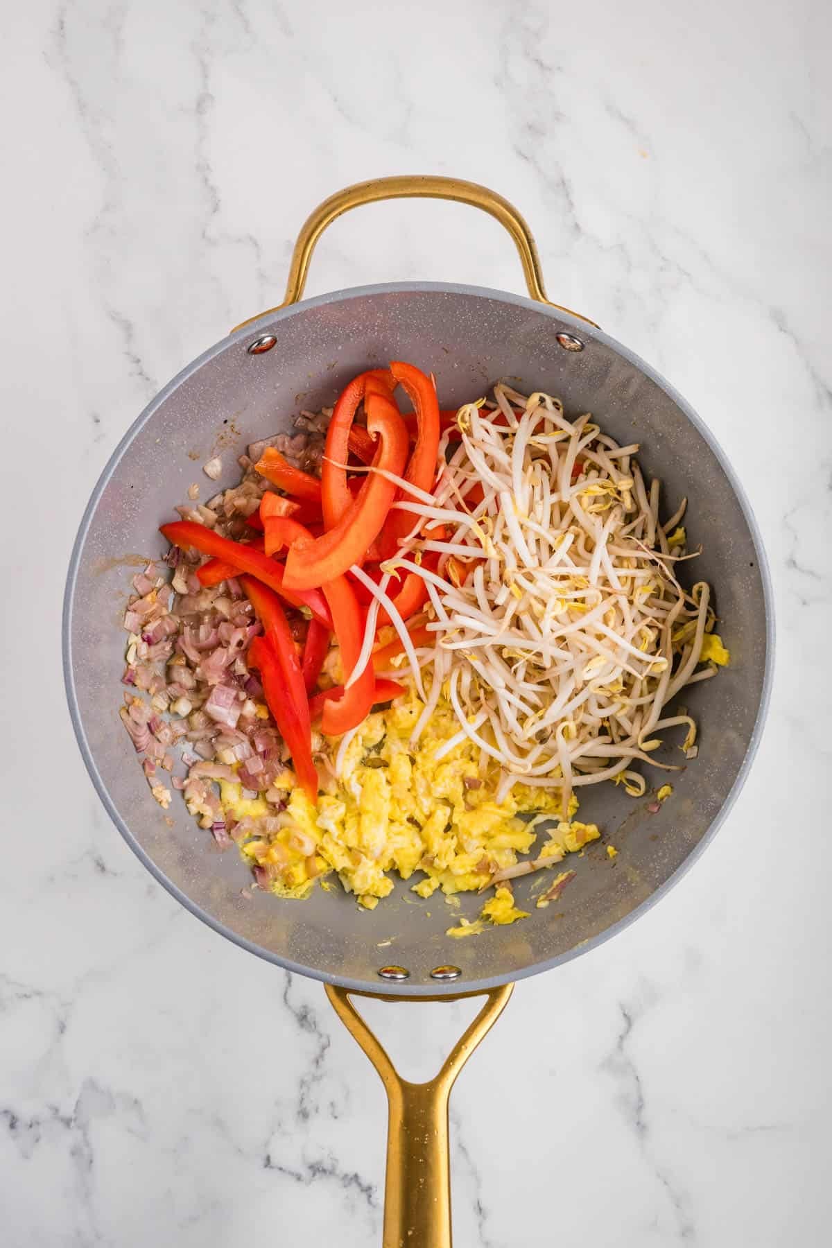 Adding veggies to a pan with cooked egg and onions.