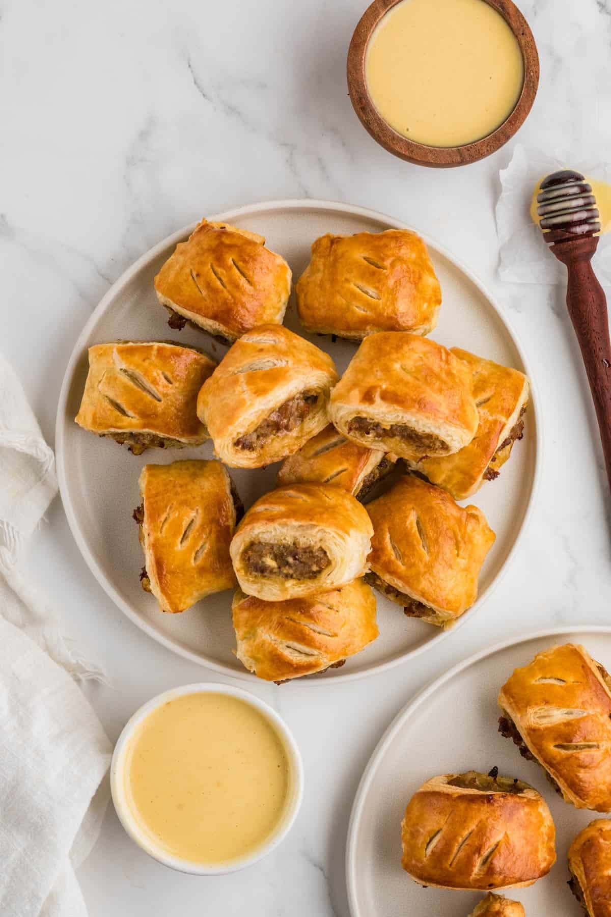 An image of sausage rolls on a plate next to bowls of honey mustard dipping sauce.
