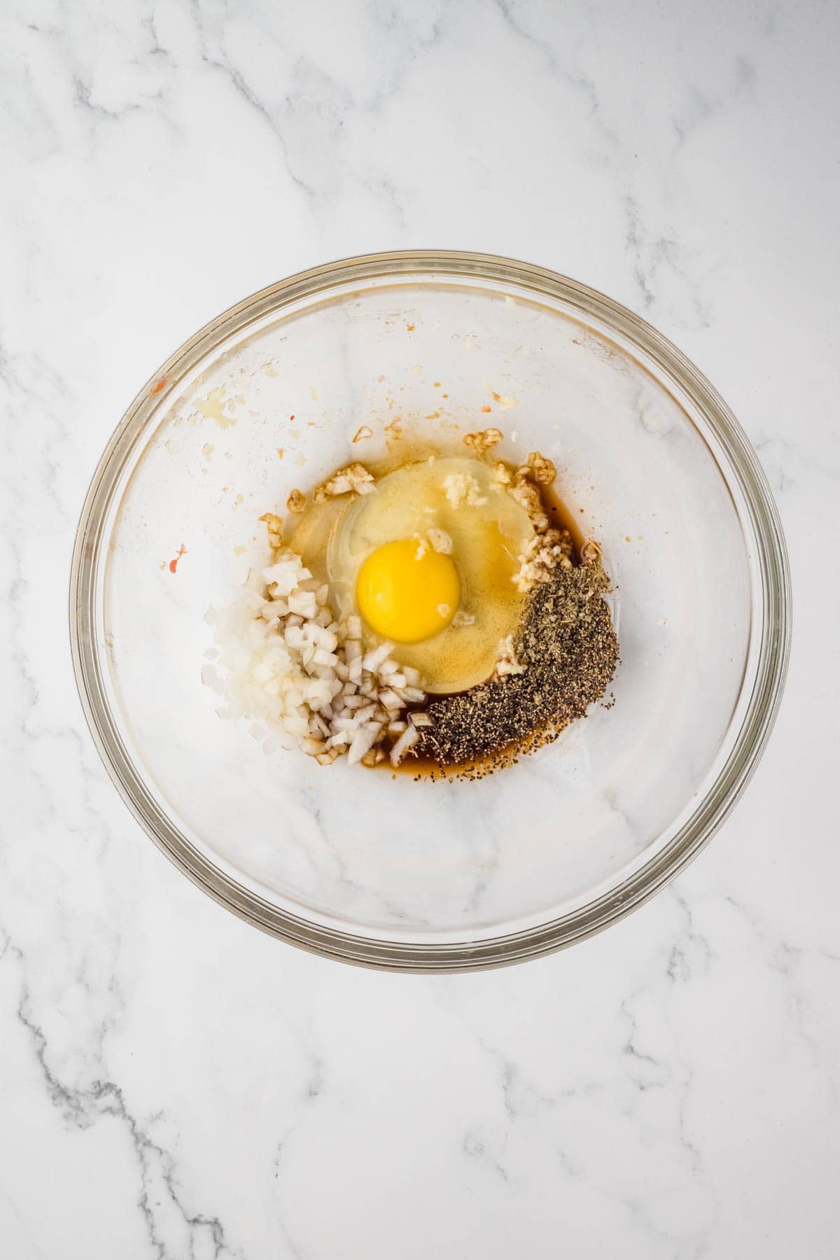 Combining an egg with seasonings and minced onion in a bowl.