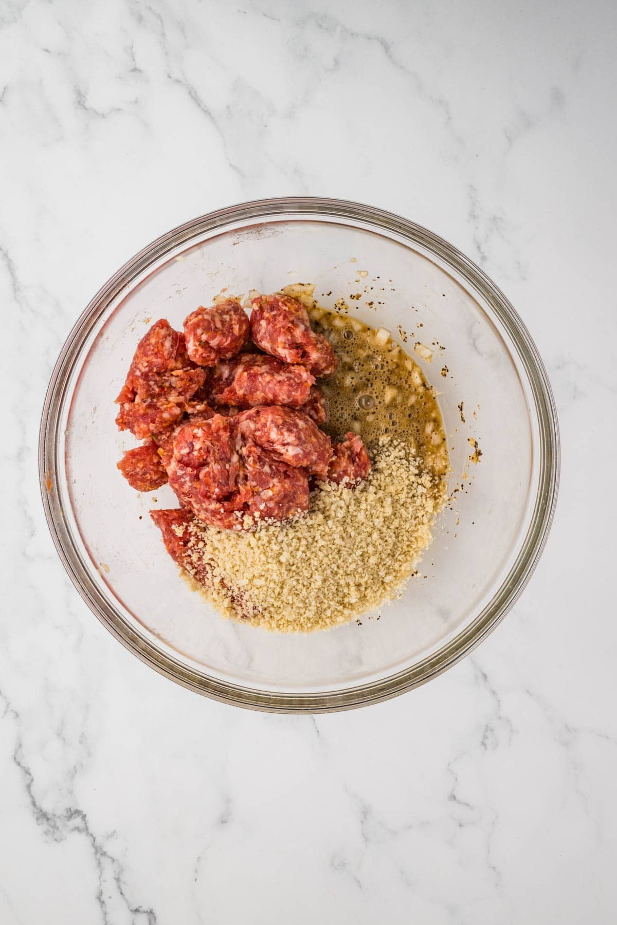 Coming uncooked Italian sausage and breadcrumbs with seasoning in a bowl.