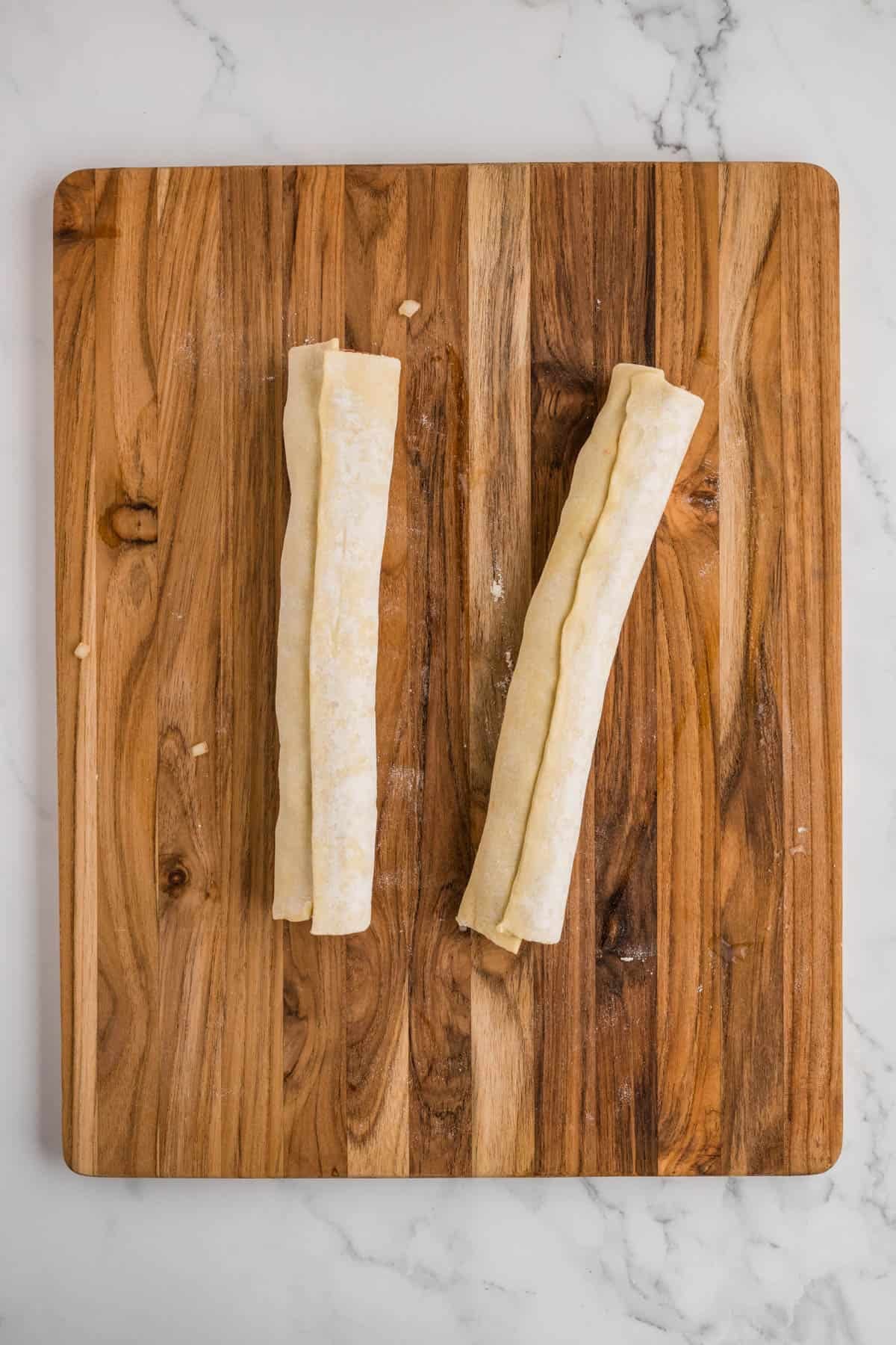 Two unbaked sausage rolls with the seams side up on a wooden cutting board.