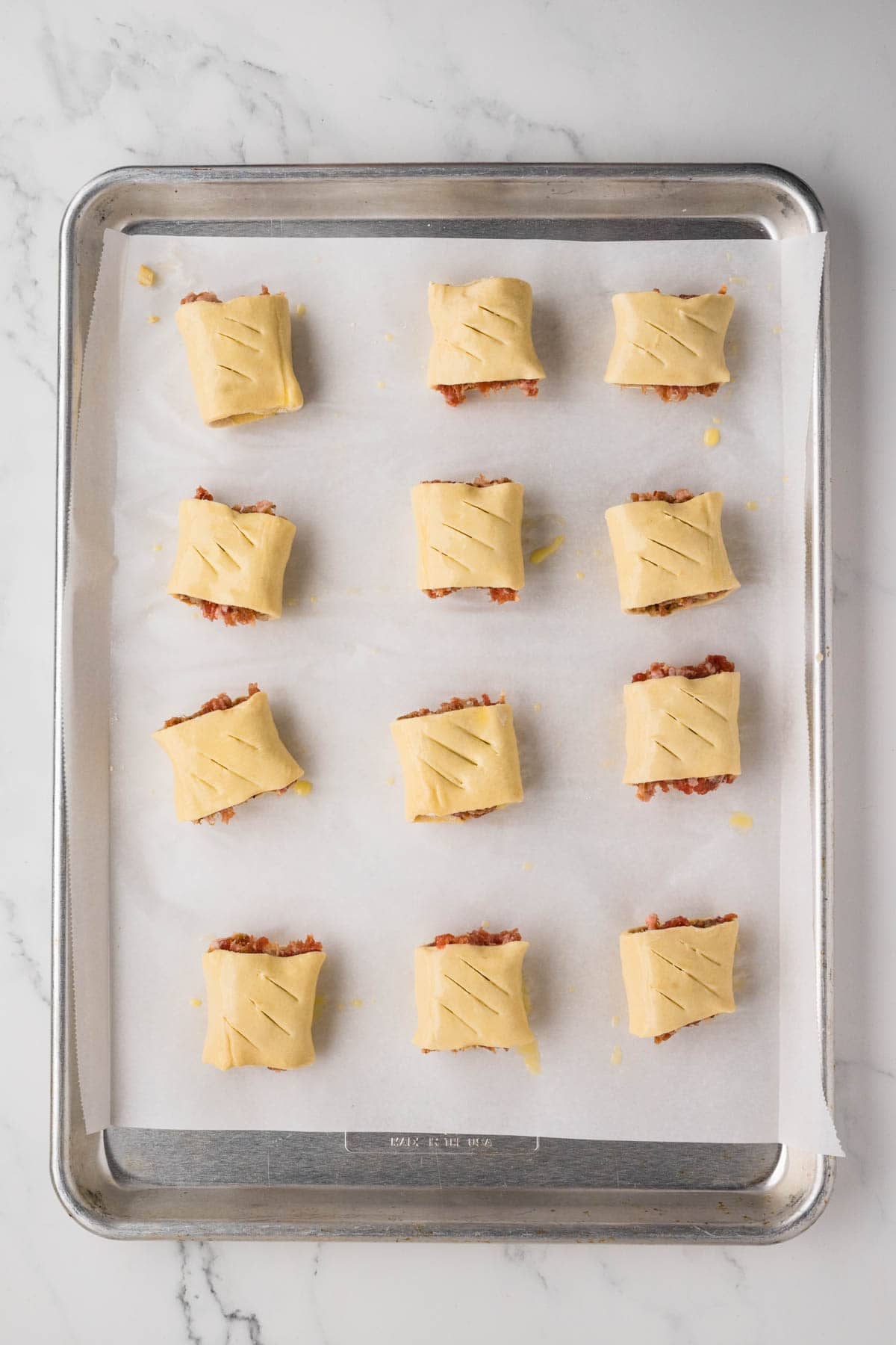 Unbaked sausage rolls on a baking sheet lined with parchment paper.