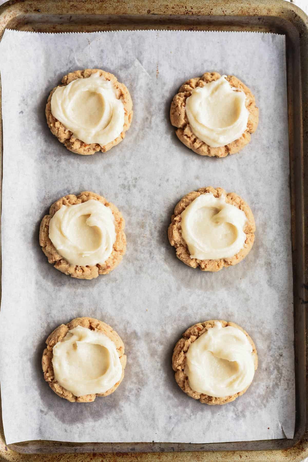 Adding creamy frosting to strawberry pretzel cookies.