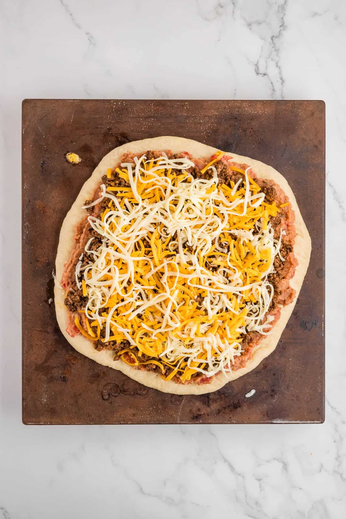 Adding shredded cheese to the top of a taco pizza.