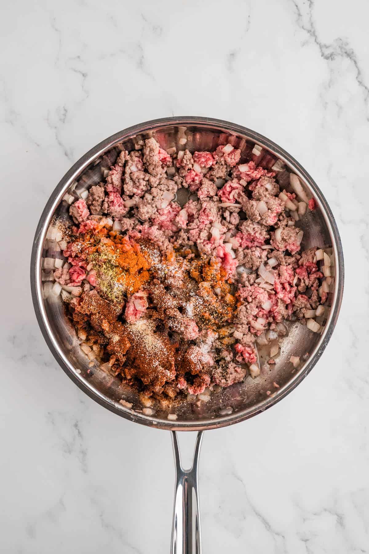 Adding spices to partially cooked ground beef in a pan.